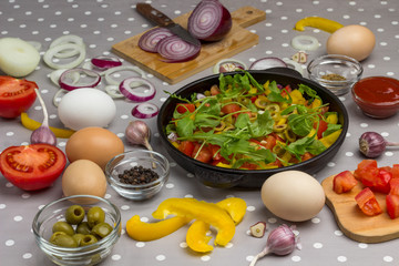 Sliced tomatoes and greens in a pan. Slicing onions on a cutting board.  .