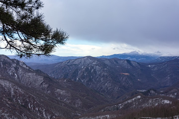 Mountain panorama in winter, snow-covered slopes, forest without leaves, gloomy state of nature.