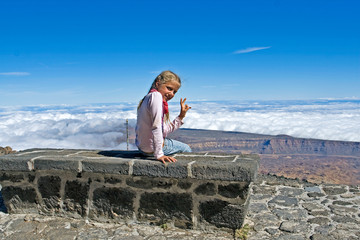 Naklejka na ściany i meble happy little girl in the clouds sits on a bench for one night stop in the Altavista mountain camp near the Teide volcano on the island of Tenerife, natural background, Spain