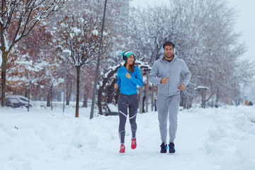 Young man and woman jogging on a snowy day in city
