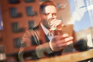 Brunet man drinking from glass sitting in cafe, reflection of building