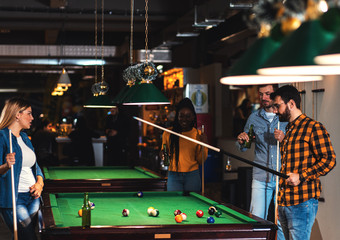 Four smiling friends in bar playing billiard together.