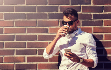 technology and people concept - young man in sunglasses with smartphone drinking coffee on city street