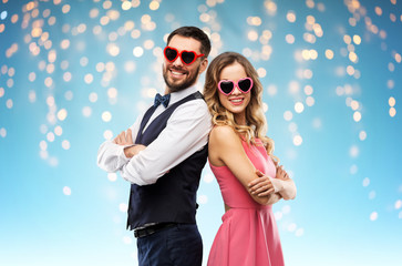valentines day, love and people concept - happy couple in heart-shaped sunglasses over holiday lights on blue background - obrazy, fototapety, plakaty