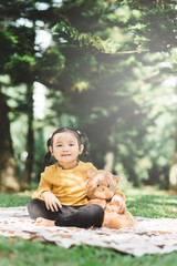 Little asian girl hugging her teddy bear in a park. Concept of happiness and childhood