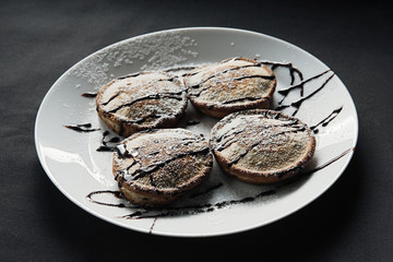 homemade chocolate pancakes served on a white plate over black texture background