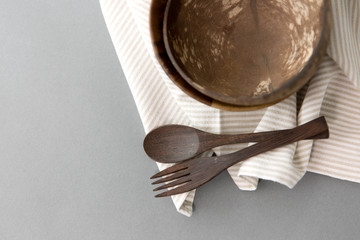 recycling, tableware and eco friendly concept - close up of coconut bowl with brown wooden spoon and fork on table