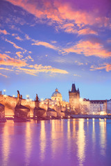 Charles Bridge reflected in Vltava river in Prague on a sunset. Vertical image with neon color toning with golden, purple, violet and blue colors.
