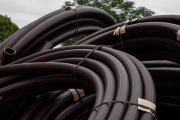 Black rubber or plastic pipes with a red lines as a construction material and equipment at building site. Using as a water pipe.