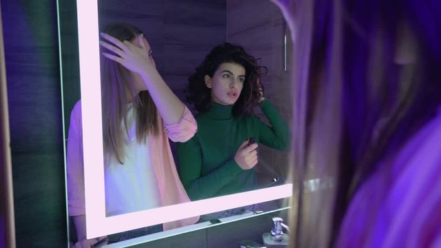 Young female friends applying makeup in front mirror, preparing for night party