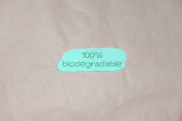 "100% biodegradable" text on and brown green packing paper background. Recycling plastic, eco friendly and zero waste concept. Flat lay, top view. 