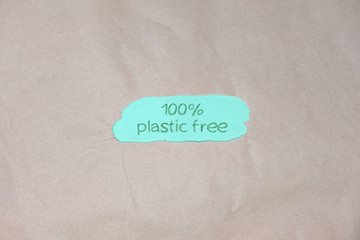 "100% plastic free" text on green and brown packing paper background. Recycling plastic, eco friendly and zero waste concept. Flat lay, top view. 