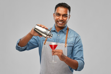 alcohol drinks, people and profession concept - indian barman in apron pouring cocktail from shaker...
