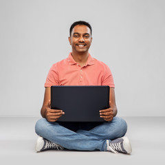 technology, internet, communication and people concept - happy indian man with laptop computer sitting on floor over grey background