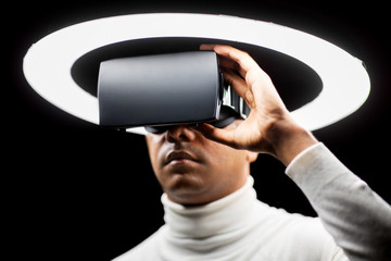 future technology, augmented reality and people concept - man in virtual reality headset or vr glasses under white illumination over black background