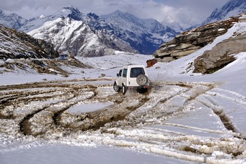 All-terrain vehicle with all-wheel drive drifting on freshly fallen snow high in the mountains of Himalayas near the track. The car creates circles on the snow with its movement.  © KrutSolt