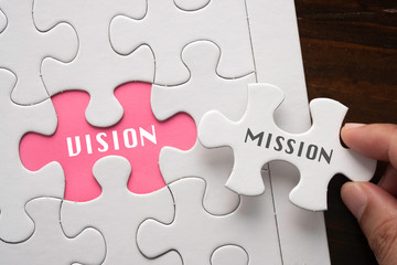 Fototapeta premium Hand hold piece of puzzle written MISSION revealing word VISION Business concept.
