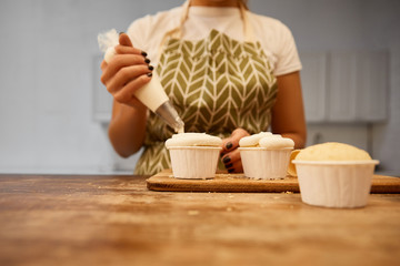 Selective focus of confectioner decorating cupcakes with cream in pastry bag, cropped view
