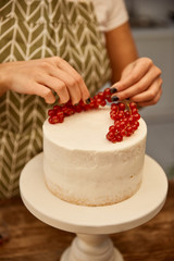 Cropped view of confectioner putting juicy redcurrant on cake with cream