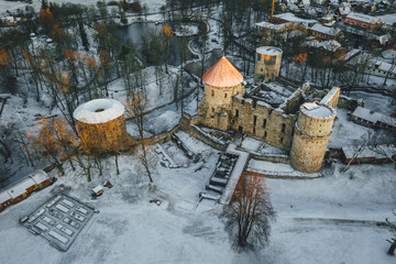 Aerial view of beautiful ruins of ancient Livonian castle in old town of Cesis, Latvia, covered in snow, winter morning sunrise time