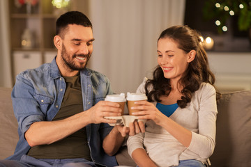 drinks, leisure and people concept - happy couple drinking takeaway tea or coffee at home in evening