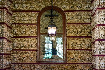 Faro, Algarve / Portugal - Skulls and bones are embedded in the wall, a lantern is lit, a crucifix behind a glass door, the Capella chapel of the Bones (Capella dos Ossos), church of Carmo