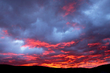 Beautiful red-blue sunset over the city with dark clouds. Dark silhouette of the city with a...