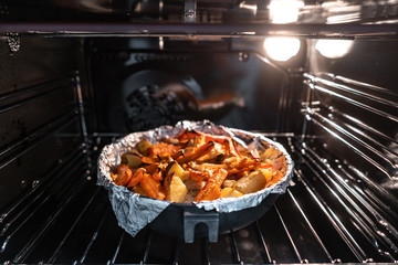 Baked potatoes with carrot and other spices in roasting pan.