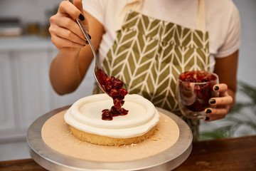 Cropped view of confectioner putting berry jam on cake
