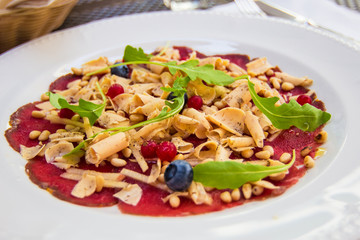 Thinly sliced deer carpaccio with pine nuts, truffles and blueberries, served on white plate, decorated. Delicious food in a typical popular restaurant in Riga, Latvia