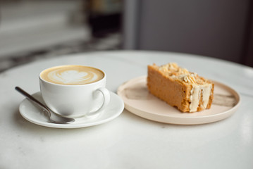 Slice of caramel cake and a fork on the right side. A cup of hot coffee with ground in the background.Close-up.