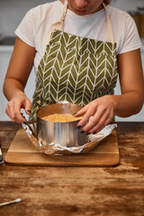 Cropped view of confectioner standing near baked cake in cake mold on foil on wooden table