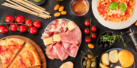 Italian food panorama. Pizza, pasta, cheese, ham, wine, olives, capers, shot from the top, a flatlay on a black background
