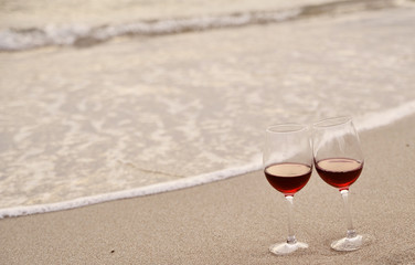 Two wine glasses with red wine on sand on the beach. Valentine's Day concept.