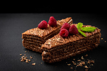 Slice of chocolate cake with milk filling and raspberry on black  background.