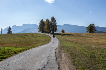 Two people hiking on a rural road on Alpe di Siusi in autumn, South Tyrol, Italy
