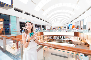 Happy Asian girl gets a marketing newsletter with discounts on her smartphone. Profitable modern shopping in the interior of the shopping center