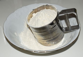 sifting flour through a sieve into a plate