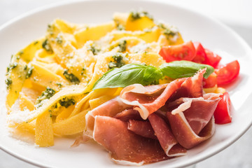 close up view of delicious Pappardelle with tomatoes, Parmesan, pesto sauce, basil and prosciutto