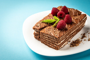 Slice of chocolate cake with milk filling and raspberry on white plate on blue background.