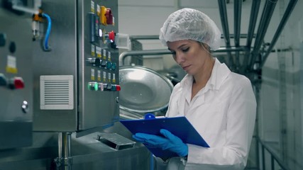 Female worker controls the quality of production equipment. One woman checks machine in a dairy facility.