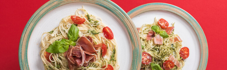 top view of cooked Pappardelle with tomatoes, basil and prosciutto on plates on red background, panoramic shot