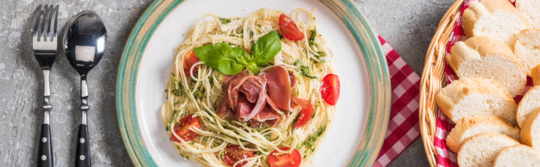 top view of served Pappardelle with tomatoes, basil and prosciutto near baguette and cutlery on...