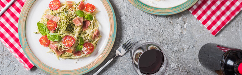 top view of Pappardelle with tomatoes, basil and prosciutto near red wine on grey surface, panoramic shot