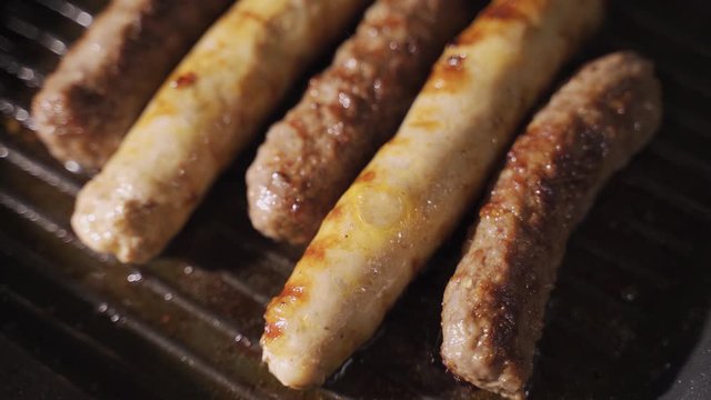 delicious grilled pork sausages rollin on hot grill pan from overhead in 4K