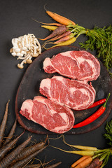 Three pieces of fresh beef meat with vegetables on wood, uncooked