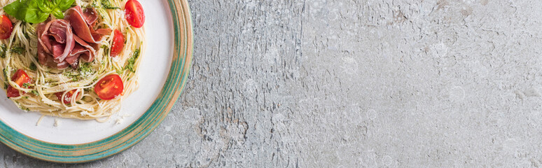 top view of Pappardelle with tomatoes, basil and prosciutto on plate on grey surface, panoramic shot