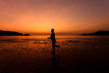 Silhouette action of a young man fun under twilight sunset sky at sea beach.