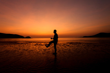 Fototapeta na wymiar Silhouette action of a young man fun under twilight sunset sky at sea beach.