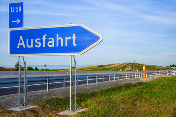 Schild mit Aufschrift Ausfahrt an einer Autobahnausfahrt mit Leitplanke und Fahrbahn.